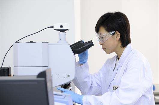 A female laboratory assistant is looking through a microscope in the technical center in Shanghai.