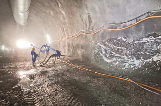 Рабочий распыляет бетон с помощью специальной установки в тоннеле.