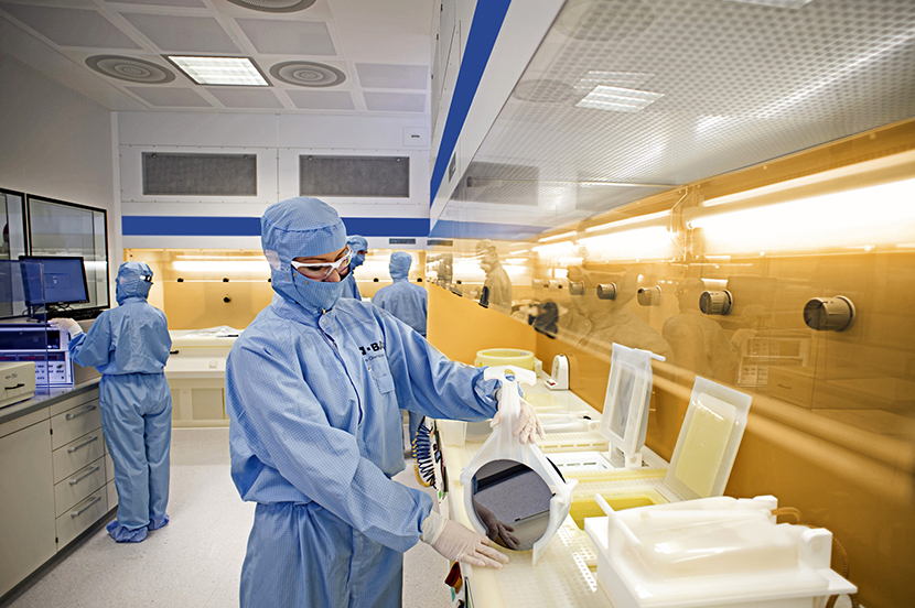 Dois assistentes de laboratório mergulham uma pastilha de silício num banho químico, composto por químicos de limpeza.